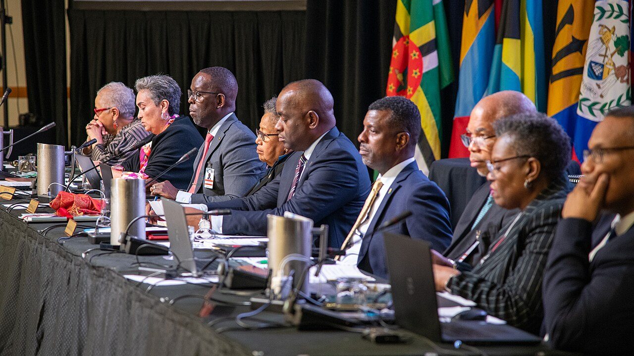 Caribbean leaders seated at a CARICOM heads of government meeting, with national flags behind them.